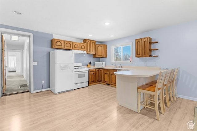 kitchen featuring light wood-style flooring, a peninsula, brown cabinets, and white appliances