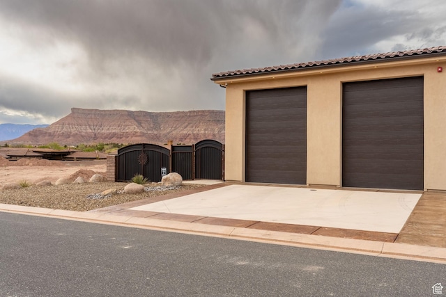 view of front of house featuring a gate, an outdoor structure, a tiled roof, a garage, and a mountain view