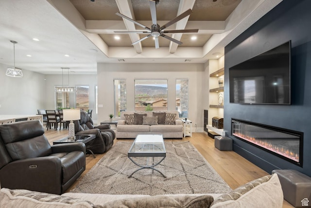 living room with light wood finished floors, a wealth of natural light, a glass covered fireplace, and a ceiling fan