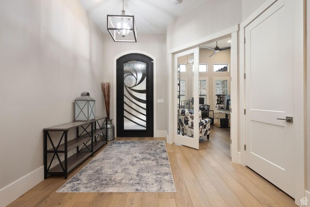 foyer entrance with baseboards, arched walkways, wood finished floors, and ceiling fan with notable chandelier