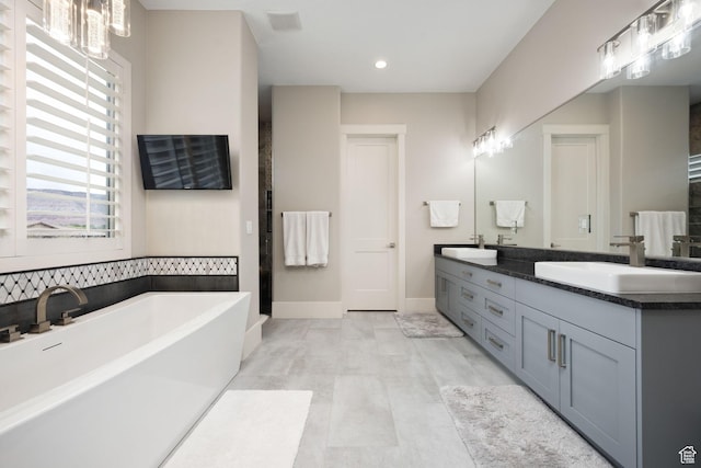 full bathroom with a soaking tub, double vanity, baseboards, and a sink