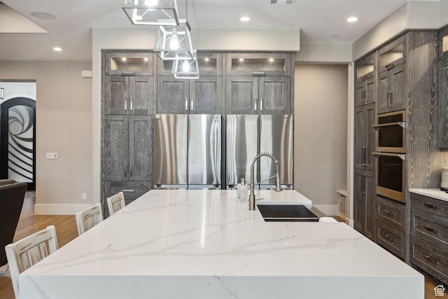 kitchen featuring a large island with sink, a sink, wood finished floors, appliances with stainless steel finishes, and recessed lighting
