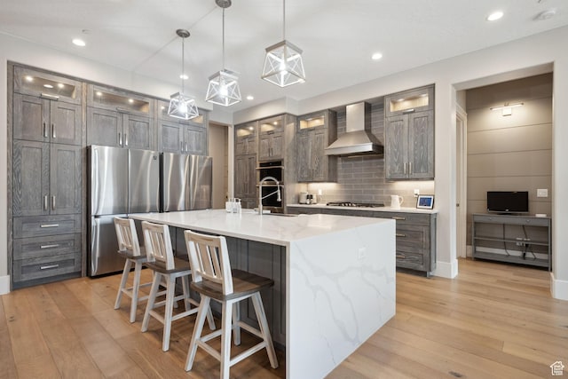 kitchen featuring light wood-type flooring, wall chimney exhaust hood, decorative backsplash, and appliances with stainless steel finishes