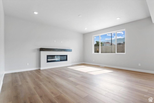 unfurnished living room featuring baseboards, recessed lighting, wood finished floors, and a glass covered fireplace