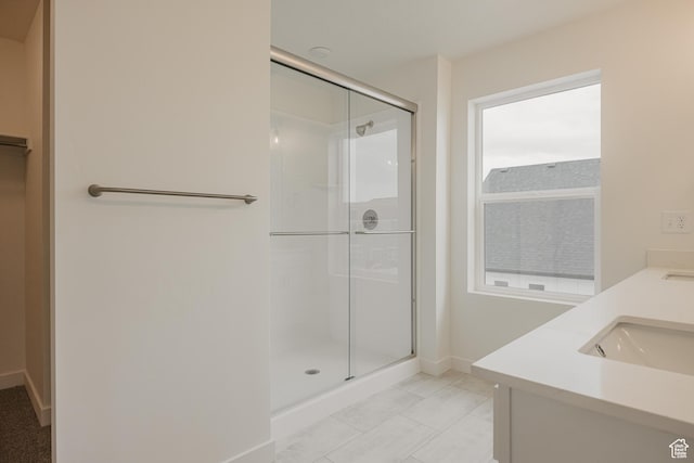 full bath featuring baseboards, double vanity, a sink, a stall shower, and tile patterned flooring