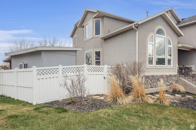 view of property exterior featuring a lawn, fence, and stucco siding