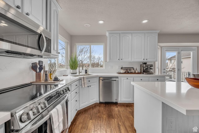 kitchen featuring dark wood-style flooring, light countertops, appliances with stainless steel finishes, white cabinetry, and a sink