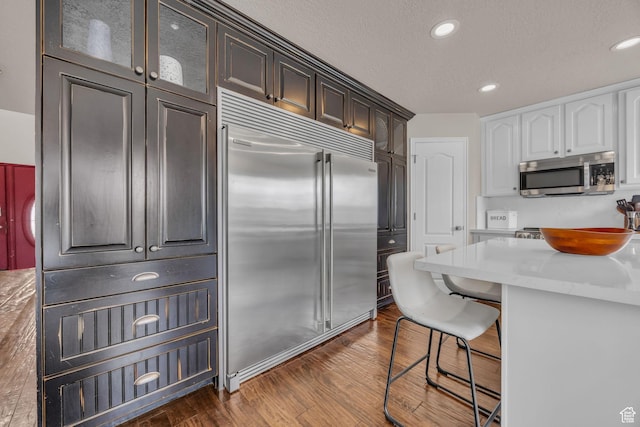kitchen featuring light countertops, dark wood-style flooring, a breakfast bar, appliances with stainless steel finishes, and glass insert cabinets
