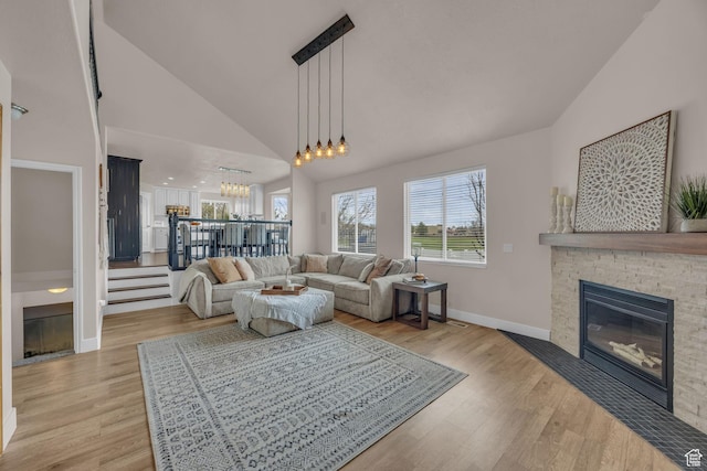 living room with light wood finished floors, a stone fireplace, baseboards, and a chandelier