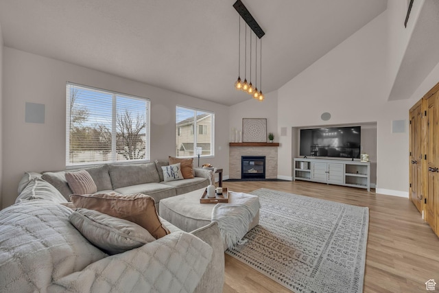 living area with high vaulted ceiling, light wood finished floors, a glass covered fireplace, baseboards, and visible vents