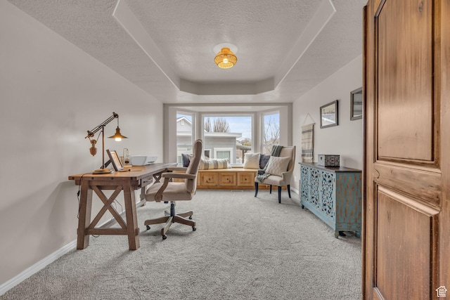 home office featuring a raised ceiling, light carpet, baseboards, and a textured ceiling