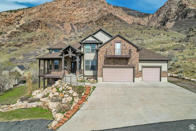 craftsman house with a mountain view, stone siding, concrete driveway, an attached garage, and a balcony