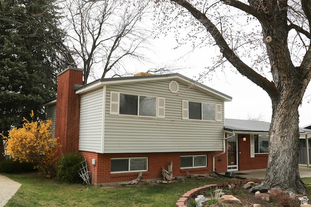 view of front of home with a front lawn, a chimney, a patio, and brick siding