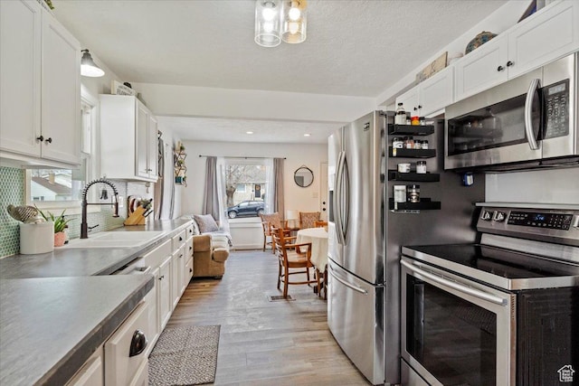 1335 Swan St, Ogden, UT 84401 - kitchen featuring light wood finished floors, stainless steel appliances, a sink, tasteful backsplash, and white cabinetry