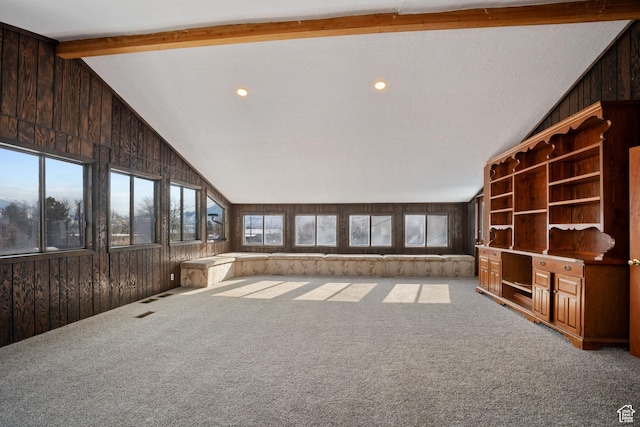 unfurnished living room with wooden walls, carpet floors, and vaulted ceiling with beams