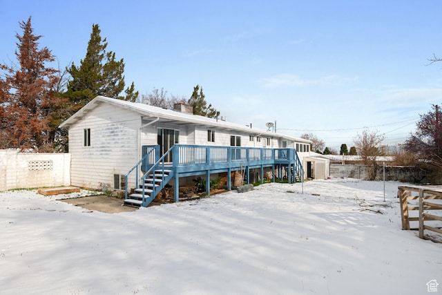 snow covered rear of property with fence, stairway, a deck, and a chimney