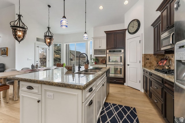 kitchen with decorative backsplash, stainless steel appliances, dark brown cabinets, a sink, and light wood-style floors