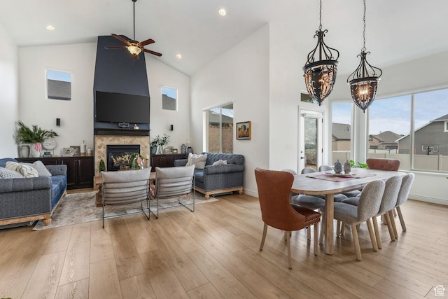 dining area featuring high vaulted ceiling, a large fireplace, light wood finished floors, baseboards, and a ceiling fan