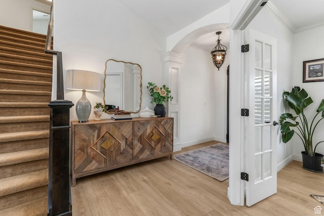 foyer entrance featuring crown molding, ornate columns, stairs, wood finished floors, and arched walkways