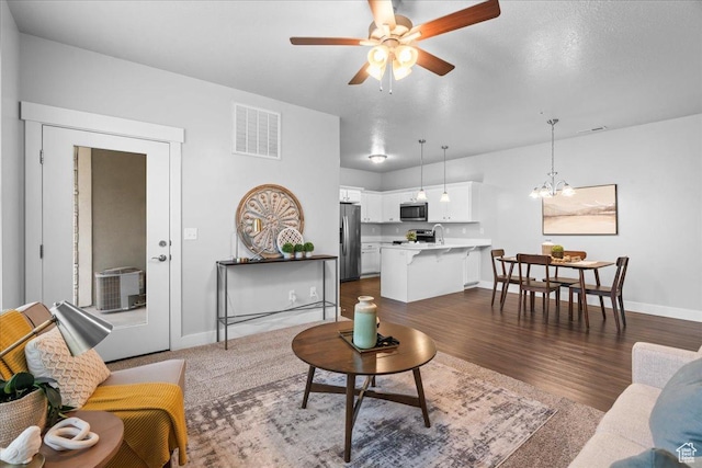 living area with dark wood-style flooring, ceiling fan with notable chandelier, baseboards, and visible vents