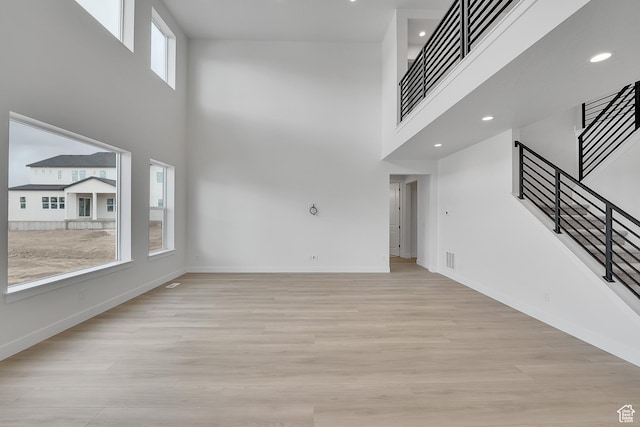 unfurnished living room featuring baseboards, stairway, a high ceiling, and light wood-style floors
