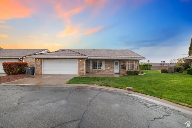 ranch-style home featuring a tiled roof, an attached garage, concrete driveway, brick siding, and a front lawn