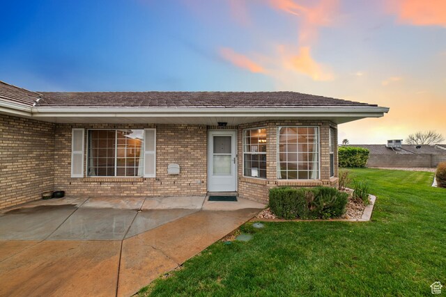 view of exterior entry featuring a lawn, brick siding, and a patio