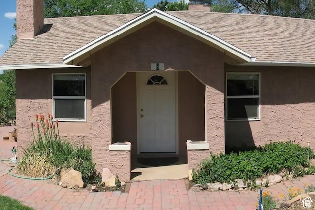 doorway to property featuring a chimney, stucco siding, and roof with shingles