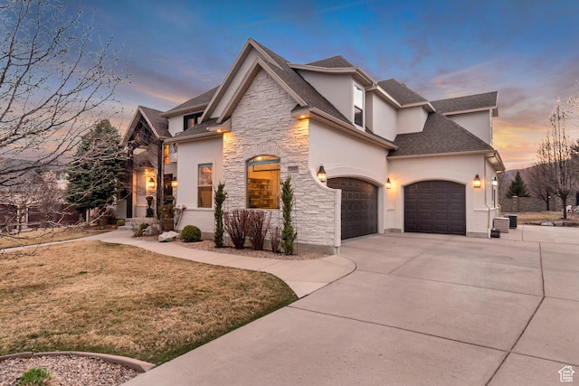 12483 N Timberline Dr, Highland, UT 84003 - property exterior at dusk featuring stone siding, roof with shingles, concrete driveway, stucco siding, and a yard