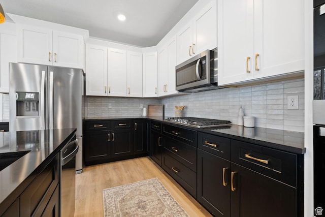 695 N Plainsman Dr Unit 110, Spanish Fork, UT 84660 - kitchen with light wood-type flooring, white cabinetry, dark cabinetry, decorative backsplash, and stainless steel appliances