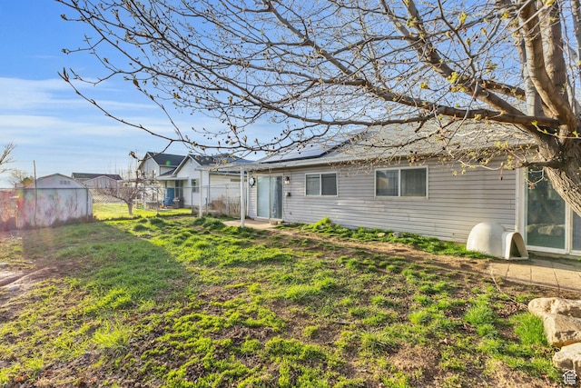 back of house featuring an outbuilding, fence, a lawn, and a storage unit