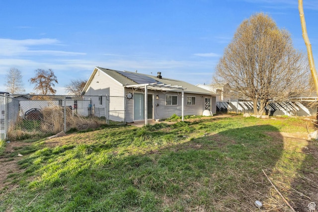 rear view of house with a fenced backyard, roof mounted solar panels, a gate, and a yard