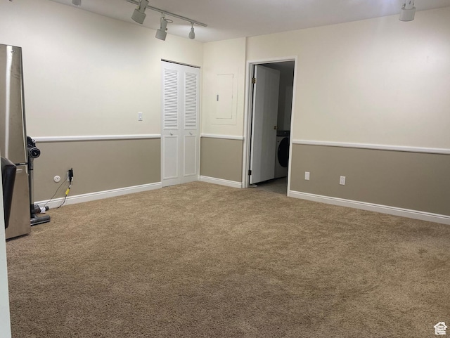 unfurnished room featuring rail lighting, carpet flooring, baseboards, and washer / dryer