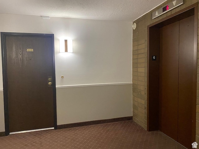 hallway with elevator, baseboards, carpet floors, and a textured ceiling