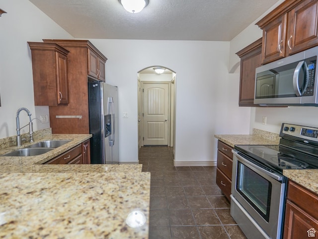 kitchen with light stone counters, a sink, a textured ceiling, stainless steel appliances, and arched walkways