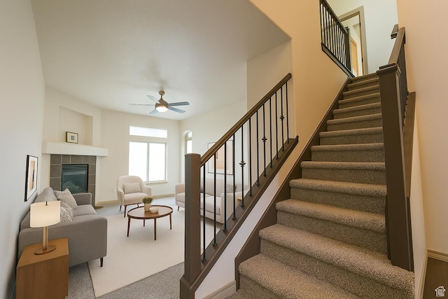 stairway with a tile fireplace, ceiling fan, baseboards, and carpet
