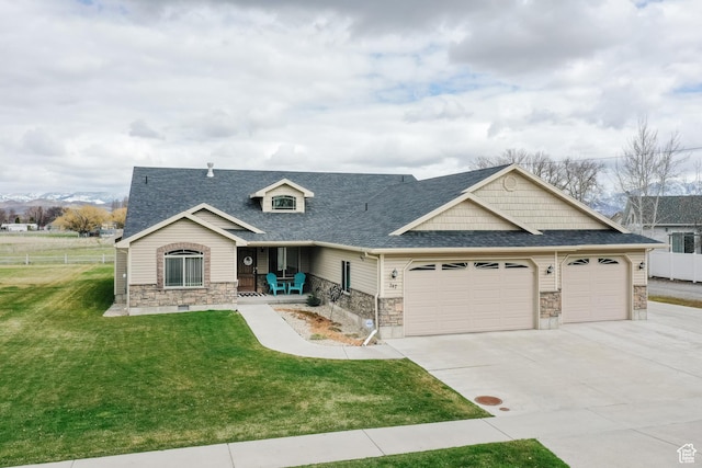 view of front of home featuring roof with shingles, an attached garage, stone siding, driveway, and a front lawn