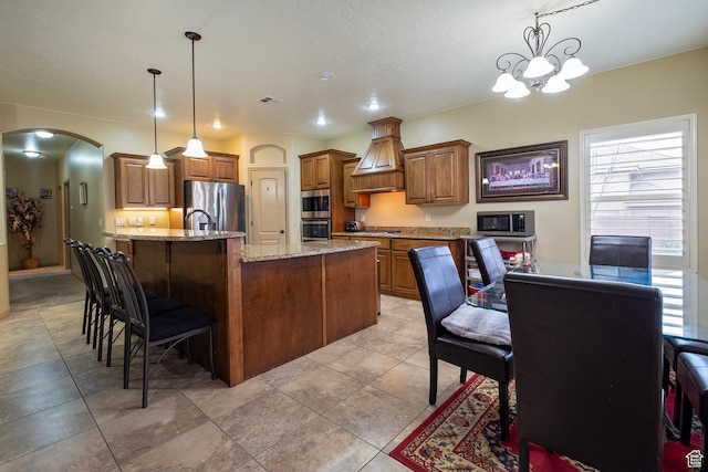 931 E Bramble Way, Washington, UT 84780 - kitchen featuring light stone countertops, brown cabinets, appliances with stainless steel finishes, arched walkways, and custom range hood