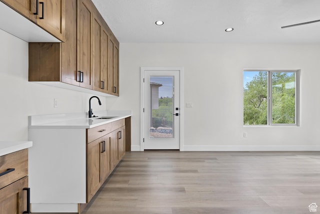 kitchen featuring light countertops, baseboards, recessed lighting, a sink, and light wood-type flooring