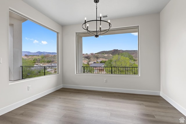 unfurnished dining area featuring an inviting chandelier, baseboards, a mountain view, and wood finished floors