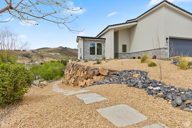 view of property exterior featuring stone siding, stucco siding, a mountain view, and an attached garage