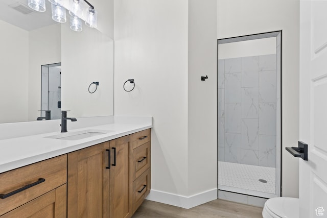 bathroom with toilet, tiled shower, vanity, wood finished floors, and visible vents