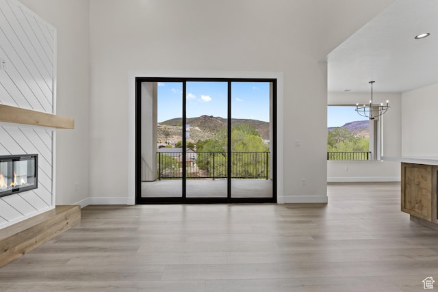 unfurnished living room with a notable chandelier, a glass covered fireplace, baseboards, and light wood-type flooring