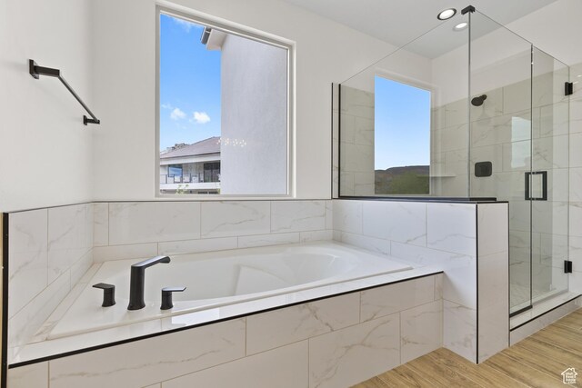 bathroom featuring wood finished floors, plenty of natural light, a garden tub, and a shower stall