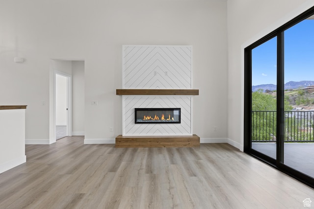 unfurnished living room with a mountain view, baseboards, wood finished floors, and a glass covered fireplace