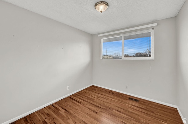 unfurnished room featuring baseboards, visible vents, wood finished floors, and a textured ceiling