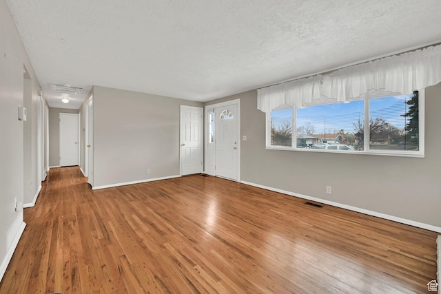 unfurnished living room featuring baseboards, a textured ceiling, light wood-style floors, and visible vents