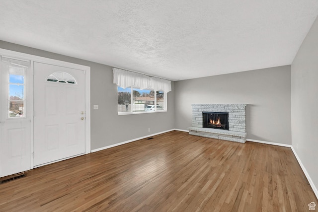 unfurnished living room with visible vents, a textured ceiling, baseboards, and wood finished floors