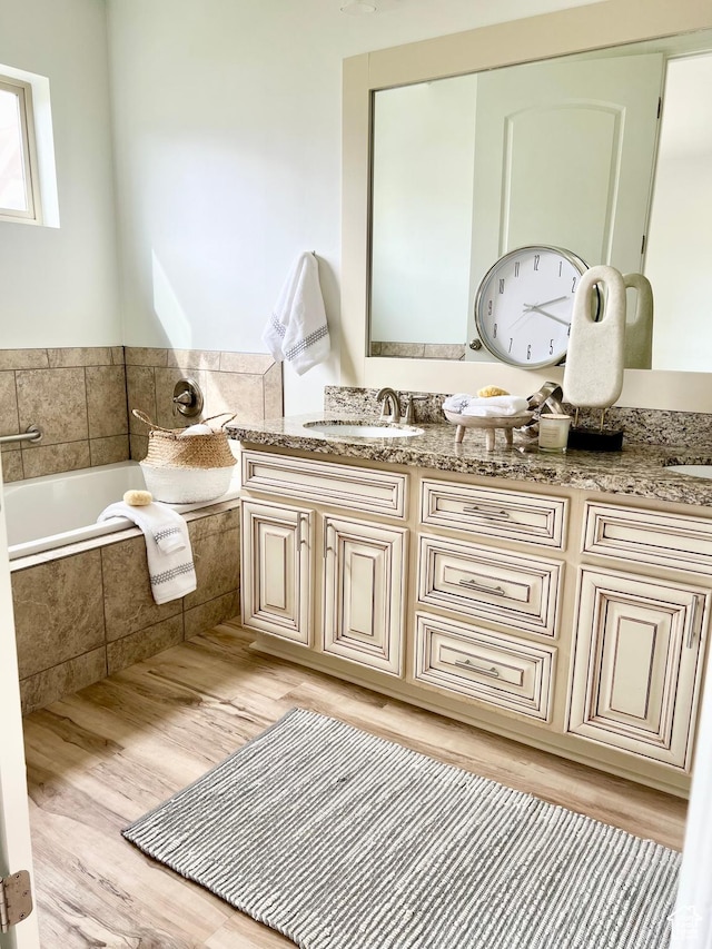 full bath featuring a sink, a bath, double vanity, and wood finished floors