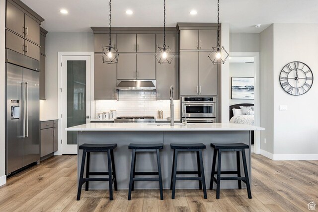 14902 S Fawley Ln, Herriman, UT 84096 - kitchen featuring backsplash, stainless steel appliances, light wood-type flooring, and under cabinet range hood